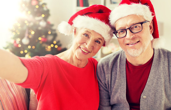 christmas, holidays and people concept - happy smiling senior couple in santa hats taking selfie at home