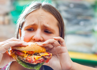 Portrait of young teenage girl eat burger. Girl trying to eat fast food