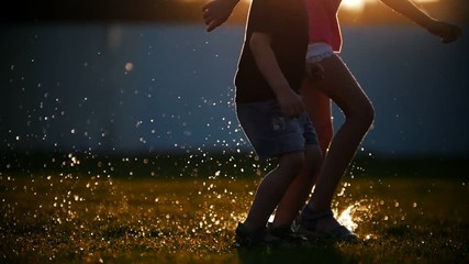 Children jump on the puddles on the grass, create a beautiful spray that glistens in the sun. Magical moment.