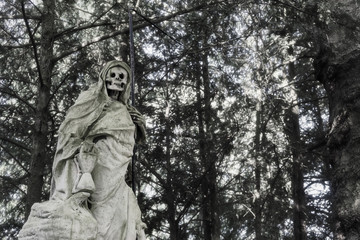 Statue of a skullfaced grim reaper made of stone with a tall scythe in his left hand.