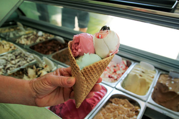 Female hand is holding a large strawberry, mint, vanilla with sour cherry ice cream in waffle cone....