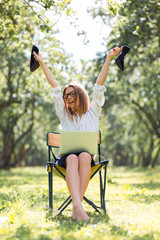 Business woman with a laptop in the Park sitting on a folding chair with her shoes in her hands