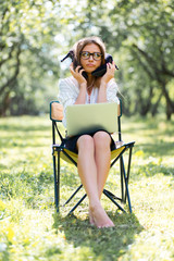 Business woman with a laptop in the Park sitting on a folding chair with her shoes in her hands