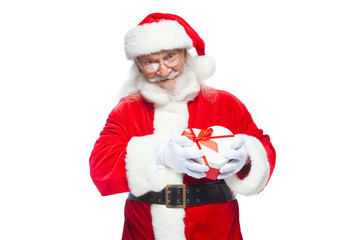 Christmas. Smiling Santa Claus in white gloves holds a red and white heart-shaped gift box with a red ribbon. Isolated on white background.