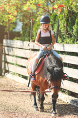 Young Caucasian girl riding on a pony, having longe line riding lesson