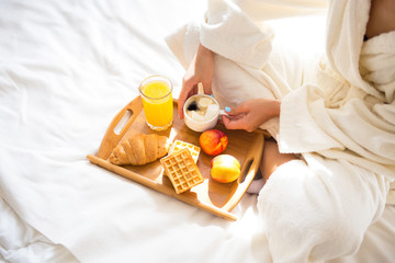 Fototapeta na wymiar beautiful brunette in a dressing gown and a sweatshirt on her head is having breakfast in bed