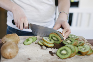 Sliced kiwi fruit sits on a cutting board with hands of a woman slicing