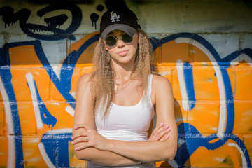 Portrait of young beautiful woman wearing white tank shirt and blue jeans and black hat on brick wall with graffiti background