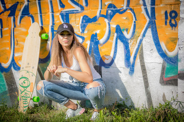 Portrait of young beautiful woman wearing white tank shirt and blue jeans and black hat on brick wall with graffiti background