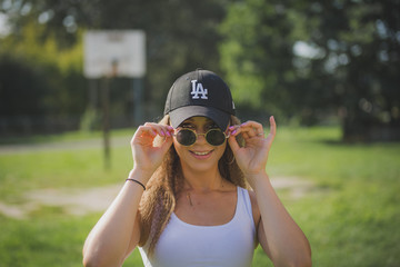 Portrait of young beautiful woman wearing white tank shirt and blue jeans and black hat on brick wall with graffiti background