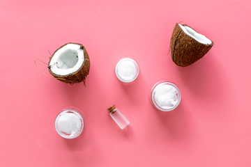 Cosmetics based on coconut oil. Oil in small bottle, cream, coconut pulp, half of coconut with shelf on pink background top view
