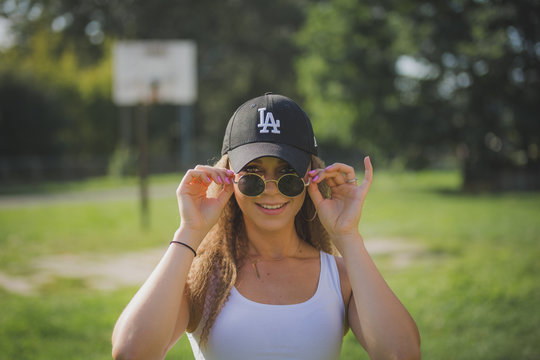 Portrait of young beautiful woman wearing white tank shirt and blue jeans and black hat on brick wall with graffiti background