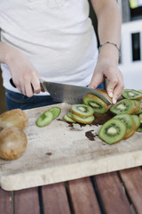 Woman slicing fresh kiwi on a wood cutting board