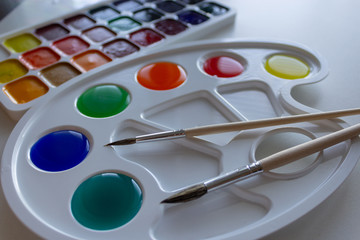 Palette with diluted multicolored paints and two brushes