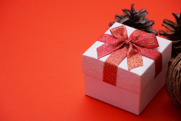 White gift box with red ribbon and pine cone with red background , have space for idea.