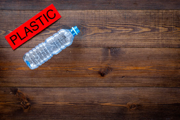 Waste suitable for recycle. Plastic bottle near word plastic on dark wooden background top view copy space