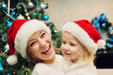 Mother and daughter in santa hat near Christmas tree