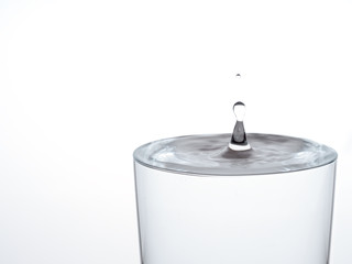 Drop of water, about to make the glass overflow and run over. On white.