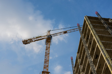 View of a conctruction building with crane on a blue sky background with clouds