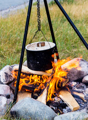 Cooking soup in black sooty saucepan on bonfire on outdoors. Authentic scene from active travel in time summer vacation.