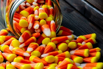 Gordijnen Halloween theme featuring a spilling of candy corn from a jar not a wooden table. © Juan Llauro