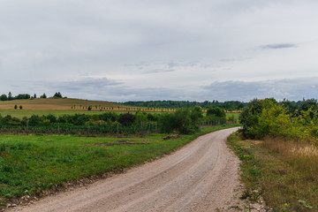 Fototapeta na wymiar Typical rural landscape design. The road leading across the field in the summer. Land of Latvia, Kurzeme region.