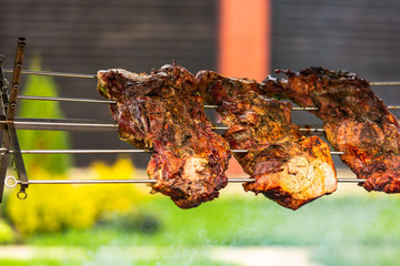 three pieces of kebab seasoned with spices are cooked on the fire near the house in a warm weather
