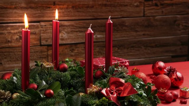 Two burning red candles on a traditional advent wreath of green fir twigs and mistletoes with festive decoration in front of a rustic wooden wall, close-up real time shot with copy space, nobody, 30s