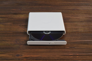 External CD/DVD/Blu-Ray Drive with opened tray and gray Blu-ray (BD) disc on light brown background (front angle view)