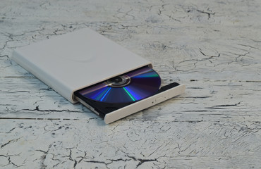 External CD/DVD/Blu-Ray Drive with opened tray and purple Blu-ray (BD) disc on white wooden...