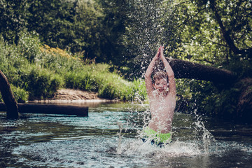 Attractive cute red-haired boy having fun, jumping, swimming and splashing in water on summer vacation