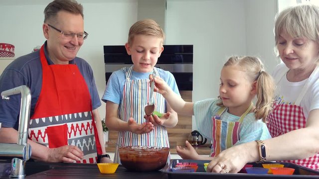 Happy grandparents have fun with their grandchildren preparing chocolate muffins at home in kitchen