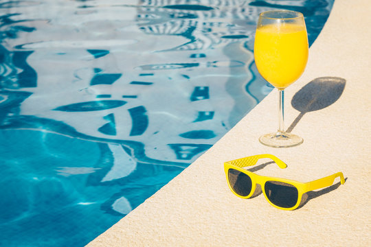 Sunglasses and a glass of juice on the poolside - girl on vacation