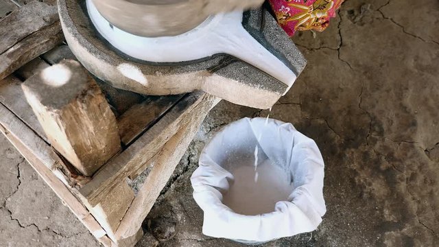 upper view on woman sat cross-legged using hand-turned millstone to grind wet rice for making soaked rice flour