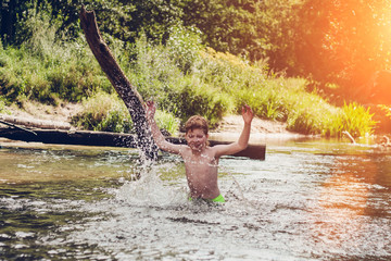 Fototapeta na wymiar Summer water fun on vacation - the boy is bathing and having fun in the river on a hot day against the backdrop of a beautiful landscape - smile, joy, happiness and positive emotions