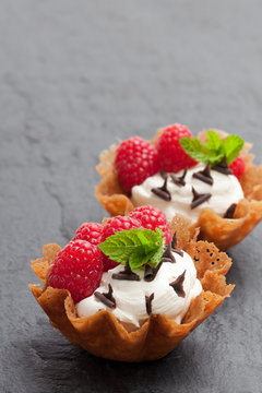 Brandy snap baskets with ice cream and berries on black stone background
