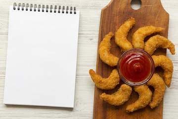 Fried shrimps tempura with sauce and blank notepad over white wooden background, top view. Space for text.