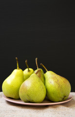 Tasty fresh pears on pink plate against black background, side view. Closeup. Selective focus. Copy space.
