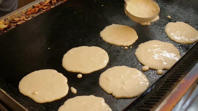 Frying pancakes on a large oven. Cook pours the dough into a large frying pan