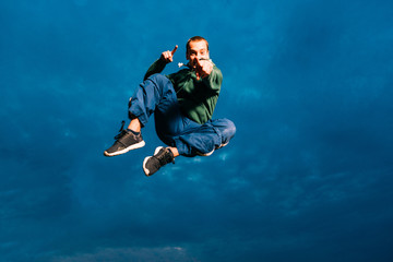 Fototapeta na wymiar Sporty man trains parkour outdoor. Young parkour man jumping in park on a sunrise against a blue sky