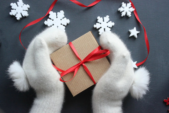 Christmas composition. Gift box with red satin ribbon holding hands in white fur mittens. Christmas decor. Extensive series of holiday pictures with various props and backgrounds. A lot of copyspace f