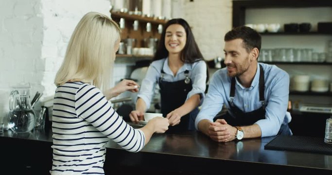 Handsome waiter talking with pretty blonde client at the bar, while waitress serving her coffee.