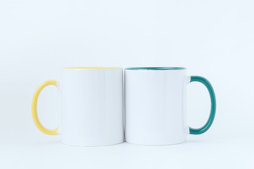 Two white mugs, with a green and yellow handle on a light background. 