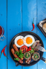 English Breakfast in a pan with fried eggs, sausages, bacon, mushrooms, jam and orange juice on wooden background copy space