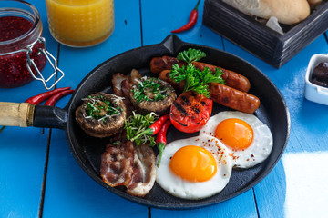 Close view English Breakfast in a pan with fried eggs, sausages, bacon, mushrooms, jam and orange juice on wooden background