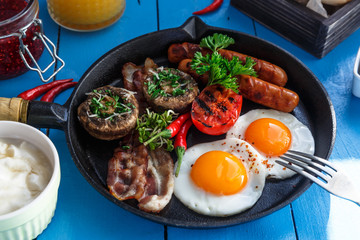 Close view English Breakfast in a pan with fried eggs, sausages, bacon, mushrooms, jam and orange juice on wooden background