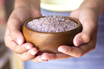 Girl's hands holding lavender bath salt in a wooden bowl