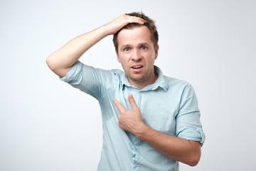 Young man in blue shirt with sweat trail on it. He is sweating becaise of hot temperature in office.