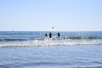 three men play volleyball by the sea