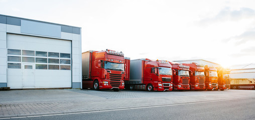 View of squadron group of new red cargo trucks parked in a row near warehouse building in bright...